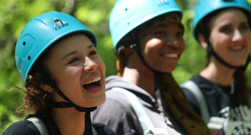 Three people wearing helmets smile. 